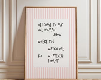 May include: A framed wall art print featuring a white background with a light pink and white vertical striped border. The text in dark gray reads: WELCOME TO MY ONE WOMAN SHOW WHERE YOU WATCH ME DO WHATEVER I WANT in a casual font.