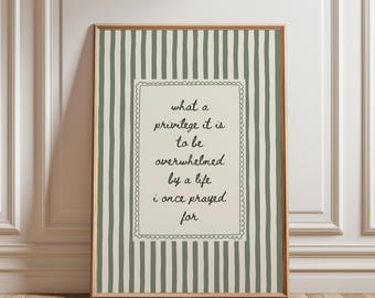 May include: A framed wall art print featuring a cream-colored central rectangle with a scalloped border, containing the black text: what a privilege it is to be overwhelmed by a life i once prayed for, set against a sage green striped background.