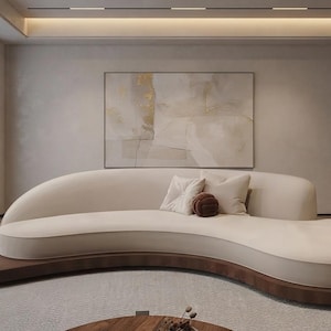 May include: A curved, cream-colored sofa with a low backrest and a smooth, upholstered seat. The sofa rests on a dark wood base that extends to form a small side table surface. Three square throw pillows are placed on the seat of the sofa.