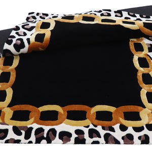 May include: A rectangular area rug featuring a central solid black square bordered by a gold-toned chain link pattern. The outer edge displays a white background with a black and brown leopard print motif, with one corner folded over to show the back.