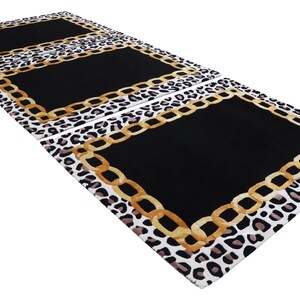 May include: A rectangular rug featuring a central solid black panel bordered by a gold-coloured chain link pattern. The outer edge of the rug displays a white, black, and brown leopard print design. The rug is shown in a repeating pattern of three.