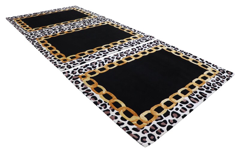 May include: A rectangular rug featuring a central solid black panel bordered by a gold-coloured chain link pattern. The outer edge of the rug displays a white, black, and brown leopard print design. The rug is shown in a repeating pattern of three.