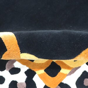 May include: A plush rug featuring a bold pattern with deep black, vibrant orange, and soft yellow sections. The surface has a thick, tufted texture, and the design includes abstract shapes and a leopard-like spotted print in black and brown tones.