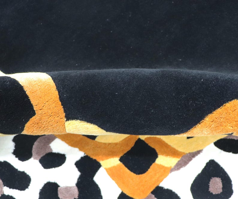 May include: A plush rug featuring a bold pattern with deep black, vibrant orange, and soft yellow sections. The surface has a thick, tufted texture, and the design includes abstract shapes and a leopard-like spotted print in black and brown tones.