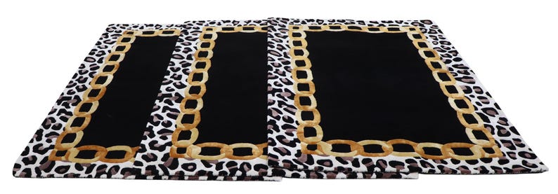 May include: Three rectangular placemats featuring a central solid black panel bordered by a gold-coloured chain link pattern. The outer edge of each placemat displays a white, black, and grey leopard print design on a rectangular fabric surface.