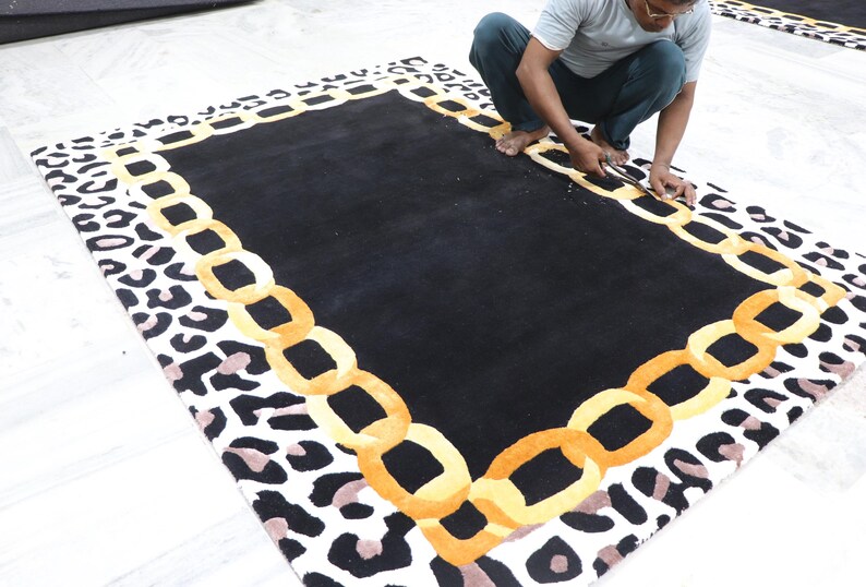 May include: A rectangular area rug featuring a solid black centre, a border composed of interlocking golden yellow chain links, and an outer edge patterned with black and light brown leopard spots on a white background.