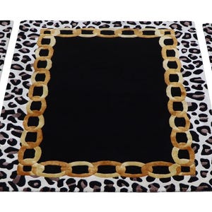 May include: Three rectangular rugs featuring a solid black centre, a gold-toned chain link border, and an outer edge with a black and white leopard print pattern. The rugs are arranged side-by-side, displaying a consistent design across all pieces.