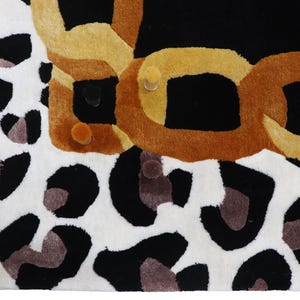 May include: A rectangular rug featuring a bold leopard print pattern in black, white, and grey tones. The design includes a prominent, thick, interlocking chain graphic rendered in shades of golden yellow and brown across the top section.