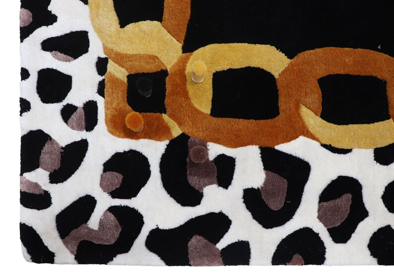 May include: A rectangular rug featuring a bold leopard print pattern in black, white, and grey tones. The design includes a prominent, thick, interlocking chain graphic rendered in shades of golden yellow and brown across the top section.