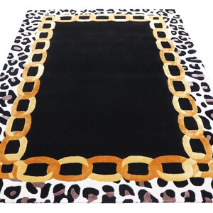 May include: A rectangular area rug featuring a solid black centre panel, a wide border composed of interlocking golden-yellow chain links, and an outer edge patterned with a black and white leopard print design on a white background.