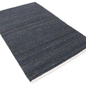 May include: A rectangular, dark blue rug with a textured surface. The rug has a white border along one edge. The rug is made of a woven material and is displayed on a white background.