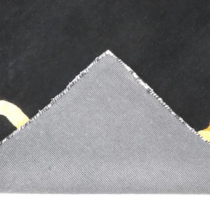 May include: A black rug with a yellow and orange chain link pattern, featuring a triangular corner folded over to reveal a grey, textured, woven backing material. The rug displays a bold graphic design with interlocking links on a dark field.