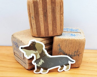 May include: A brown and grey dachshund dog sticker with a white outline. The sticker is placed on top of a stack of wooden blocks.