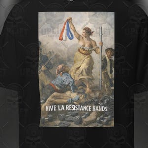 Può includere: T-shirt nero con una stampa di un dipinto classico raffigurante una donna che tiene una barra e nastri rossi, bianchi e blu. Il testo "VIVE LA RESISTANCE BANDS" è sotto l'immagine. La maglietta ha un girocollo e maniche corte.