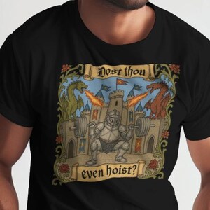 May include: Black t-shirt featuring a medieval-themed graphic. The design includes a knight lifting weights in front of a castle, with dragons and the text "Dost thou even hoist?" in a scroll.