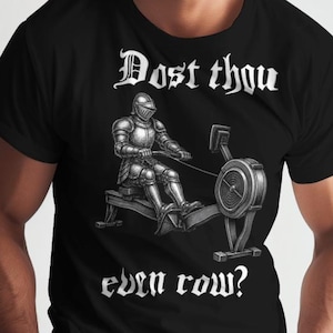 May include: Black t-shirt with a graphic of a knight in armor on a rowing machine, with the text "Dost thou even row?" in white. The design is a humorous take on fitness and medieval themes.