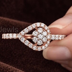 May include: A rose gold ring featuring a pear-shaped halo design with a cluster of small round white stones in the center. The band and the pear-shaped frame are encrusted with tiny white stones. The text EverGlowJewls is visible on the left.
