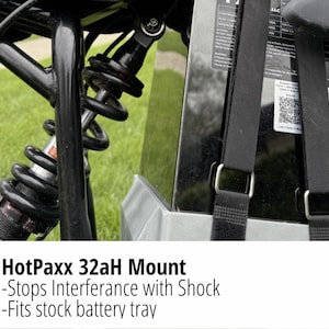 May include: Close-up of a black suspension system with a silver spring and red accents. The image also shows a black battery mount with black straps and the text "HotPaxx 32aH Mount - Stops Interference with Shock - Fits stock battery tray."