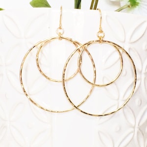 May include: Gold-toned double hoop earrings with a hammered texture. The earrings are made of two interlocking hoops, one slightly larger than the other.