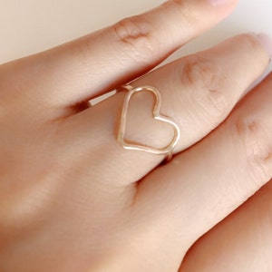May include: A gold-toned ring with a heart-shaped design. The ring is worn on a finger.
