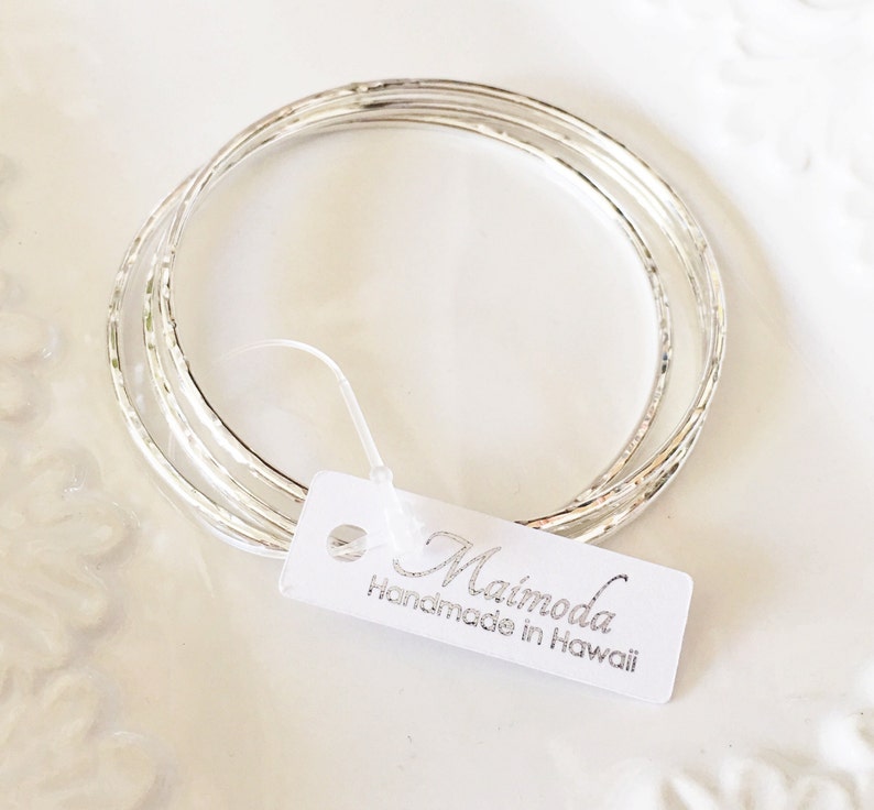 Peut inclure: Ensemble de quatre bracelets en argent avec une texture martel&eacute;e. Les bracelets sont empil&eacute;s les uns sur les autres et ont une finition brillante. L'&eacute;tiquette attach&eacute;e aux bracelets indique "Maimoda Handmade in Hawaii".