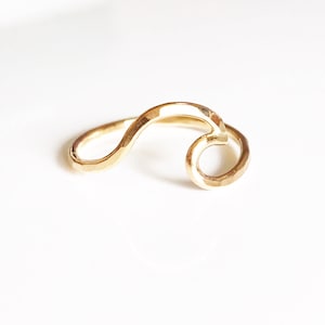May include: A gold-colored ring with a flowing, wave-like design. The ring has a hammered texture and a smooth, polished finish. The ring is a piece of jewelry.