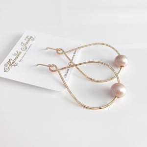 May include: Gold teardrop earrings with a pearl accent. The earrings are handmade and feature a 14k gold filled wire.