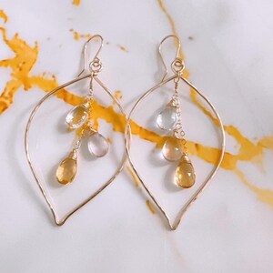 May include: Gold leaf-shaped earrings with dangling clear and yellow gemstones.