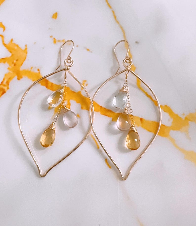 May include: Gold leaf-shaped earrings with dangling clear and yellow gemstones.