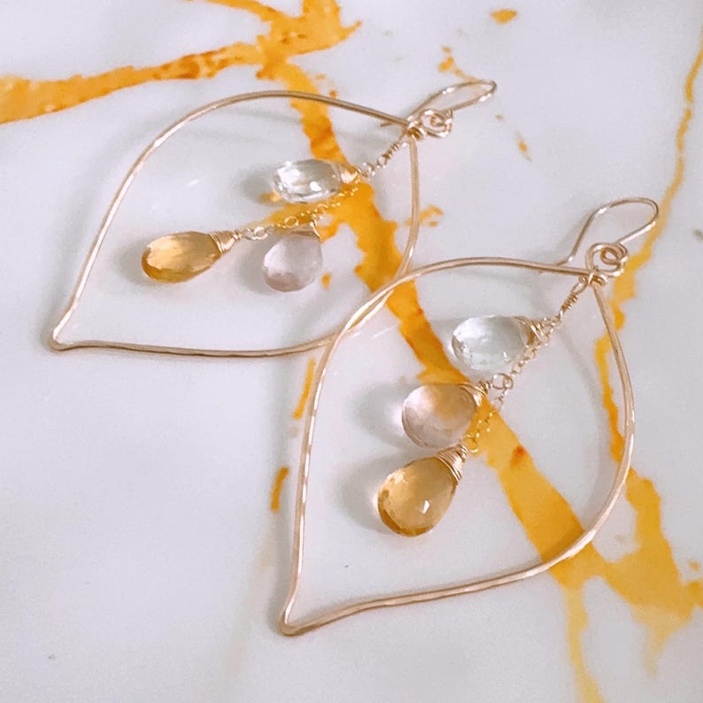 May include: Gold tone earrings with a teardrop shape and dangling stones. The stones are clear, light pink, and yellow.