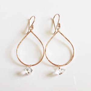 May include: Rose gold teardrop earrings with a clear crystal dangling from each earring.