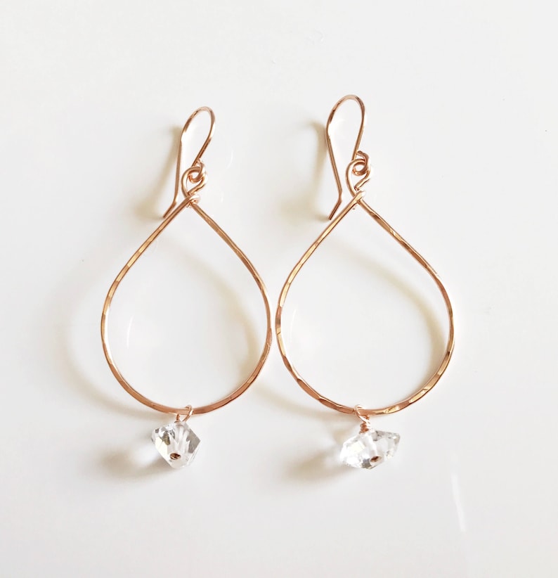 May include: Rose gold teardrop earrings with a clear crystal dangling from each earring.