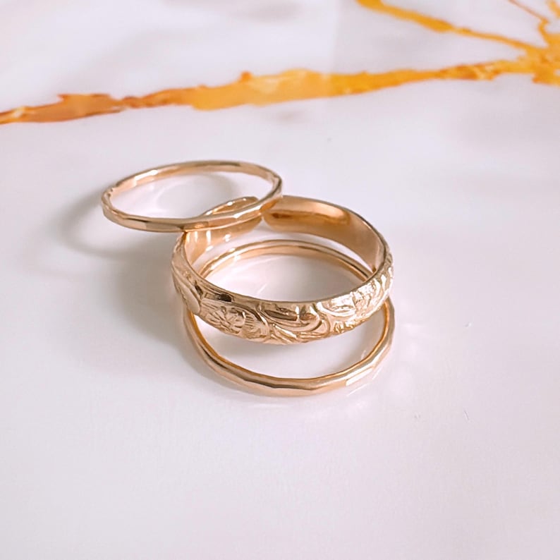 Op de afbeelding: Set van drie gouden ringen. De middelste ring heeft een bloemenmotief. De andere twee ringen zijn simpel.