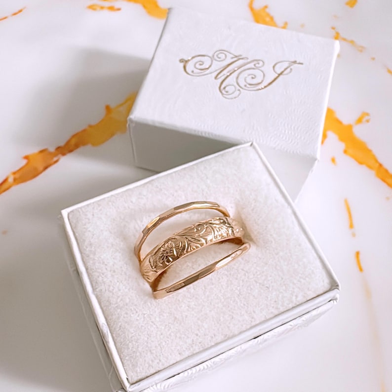 Op de afbeelding: Een gouden ringset met drie banden, waarvan &eacute;&eacute;n met een bloemenmotief, in een witte doos met de initialen "MJ" op de deksel.