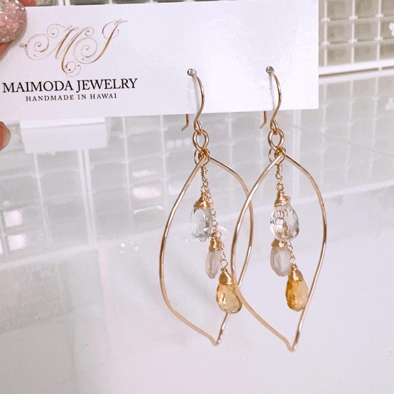 May include: Gold leaf earrings with a delicate wire design and dangling gemstones. The earrings feature clear, pink, and yellow gemstones.