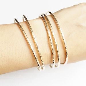 May include: Five gold-toned hammered metal bangles stacked on a wrist.