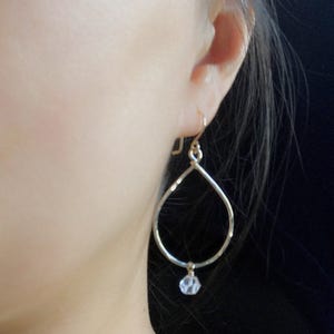 May include: Gold teardrop shaped earrings with a clear crystal dangling from the bottom.