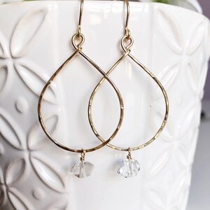 May include: Gold teardrop earrings with a clear crystal charm hanging from each earring.