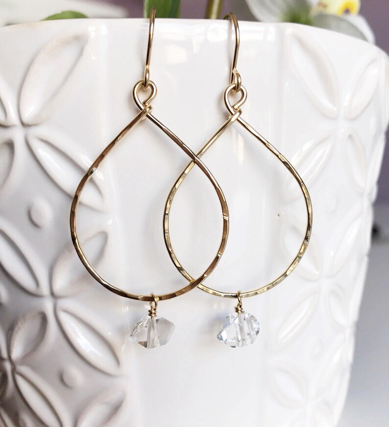 May include: Gold teardrop earrings with a clear crystal charm hanging from each earring.