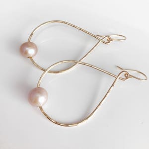 May include: Gold teardrop shaped hoop earrings with a single pearl on each hoop.