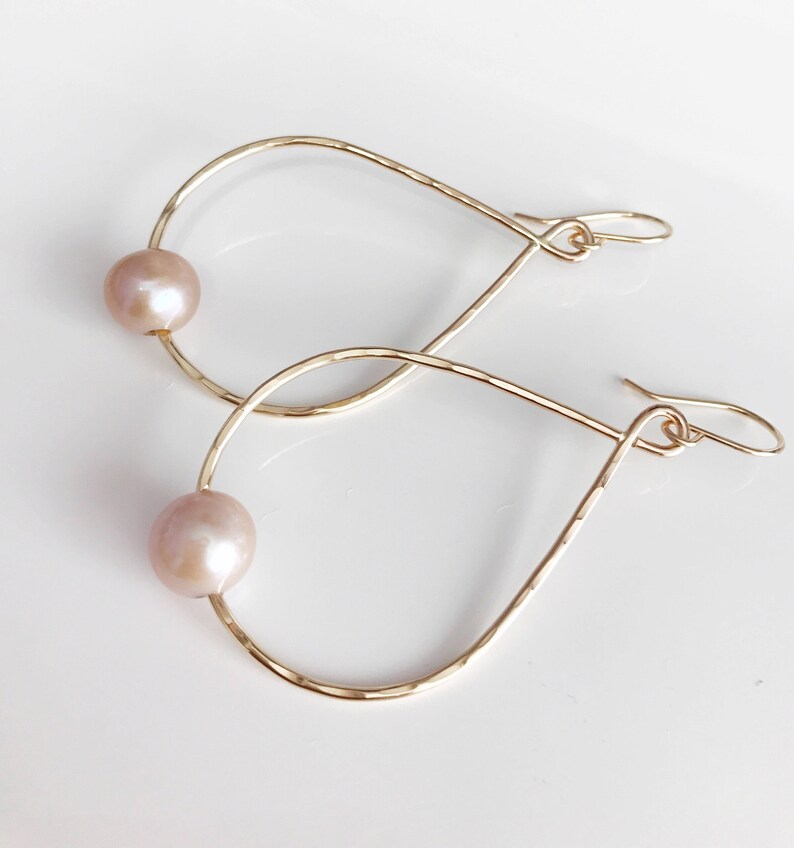 May include: Gold teardrop shaped hoop earrings with a single pearl on each hoop.