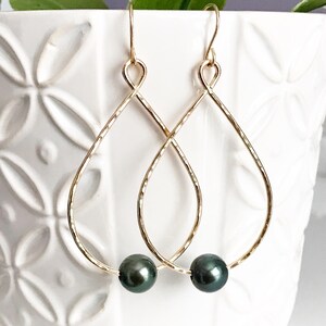 May include: Gold teardrop earrings with a black pearl dangling from each earring.