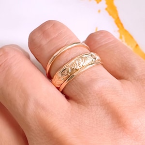 Op de afbeelding: Drie gouden ringen gestapeld op een vinger. De bovenste ring heeft een bloemmotief.