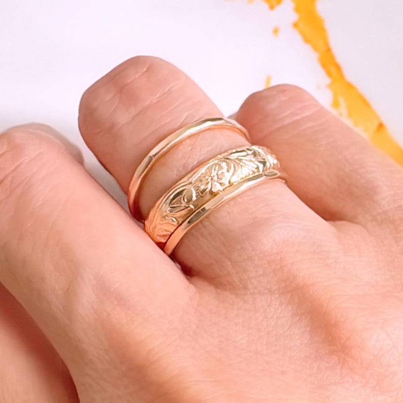 Op de afbeelding: Drie gouden ringen gestapeld op een vinger. De bovenste ring heeft een bloemmotief.