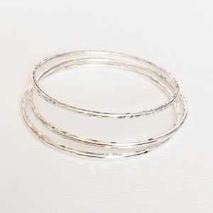 Peut inclure: Trois bracelets en argent empil&eacute;s les uns sur les autres. Les bracelets sont tous lisses et ont une texture martel&eacute;e.