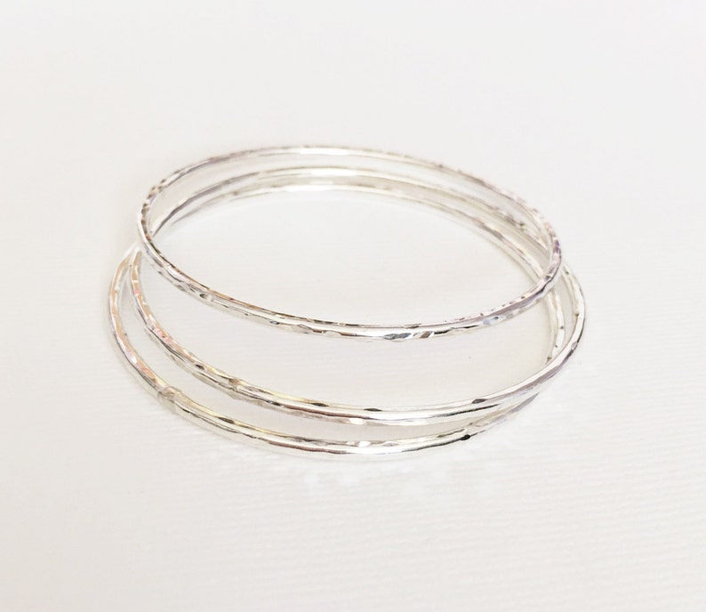 Peut inclure: Trois bracelets en argent empil&eacute;s les uns sur les autres. Les bracelets sont tous lisses et ont une texture martel&eacute;e.