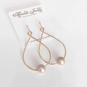 May include: Gold-filled teardrop earrings with a pink pearl accent. The earrings are handmade in Hawaii by Maimoda Jewelry.
