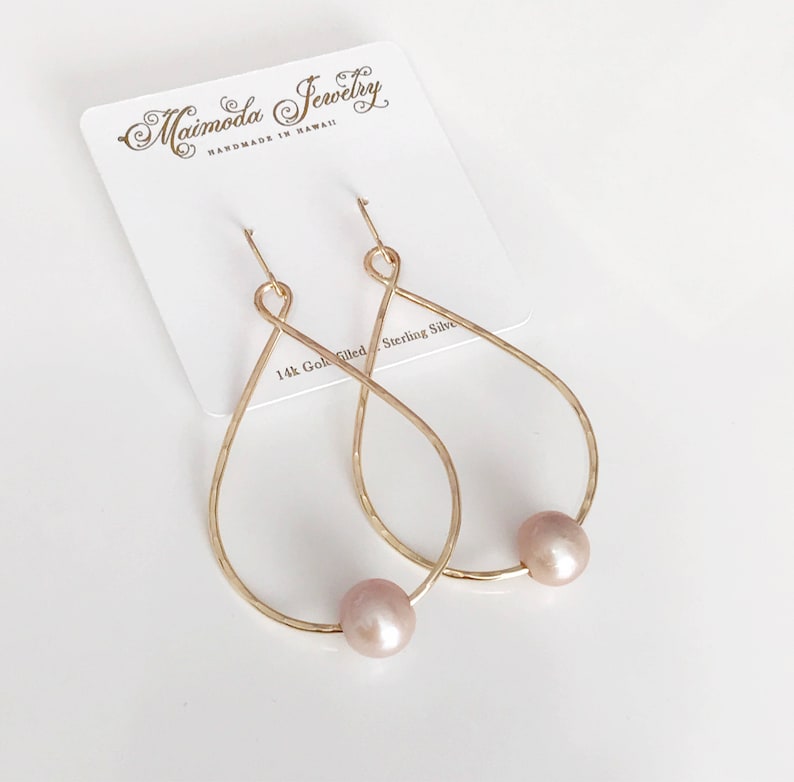 May include: Gold-filled teardrop earrings with a pink pearl accent. The earrings are handmade in Hawaii by Maimoda Jewelry.