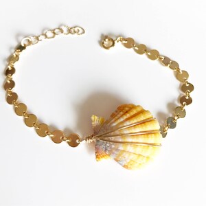 May include: A gold chain bracelet with a yellow seashell charm. The chain is made of small, round links.