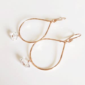 May include: Rose gold teardrop earrings with clear crystal accents. The earrings are made of hammered metal and have a delicate, feminine look.